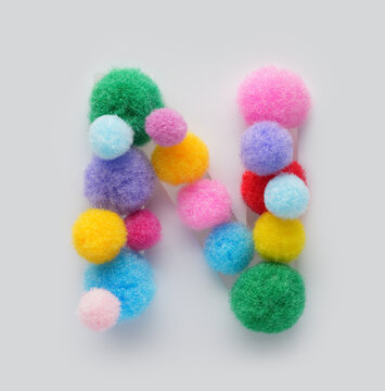 Colorful letter N made of fluffy pom poms on white background. Creative handmade typography for kids learning alphabet, educational design, playful classroom decor, and graphic projects.