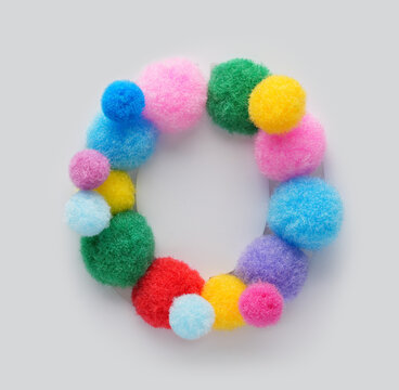 Colorful letter O made of fluffy pom poms on white background. Creative handmade typography for kids learning alphabet, educational design, playful classroom decor, and graphic projects.