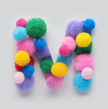 Colorful letter M made of fluffy pom poms on white background. Creative handmade typography for kids learning alphabet, educational design, playful classroom decor, and graphic projects.
