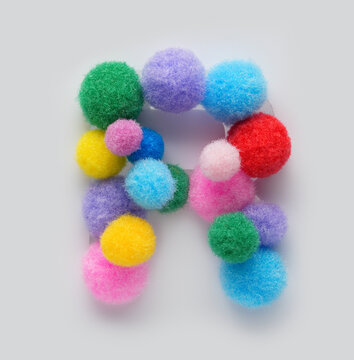 Colorful letter R made of fluffy pom poms on white background. Creative handmade typography for kids learning alphabet, educational design, playful classroom decor, and graphic projects.