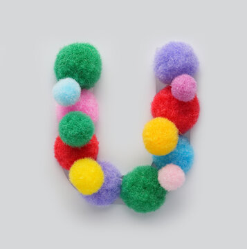 Colorful letter U made of fluffy pom poms on white background. Creative handmade typography for kids learning alphabet, educational design, playful classroom decor, and graphic projects.