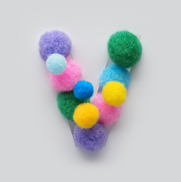 Colorful letter V made of fluffy pom poms on white background. Creative handmade typography for kids learning alphabet, educational design, playful classroom decor, and graphic projects.