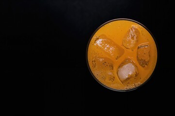 Obraz premium Chilled Orange Beverage with Ice Cubes on a Black Surface, Overhead Shot with Empty Space