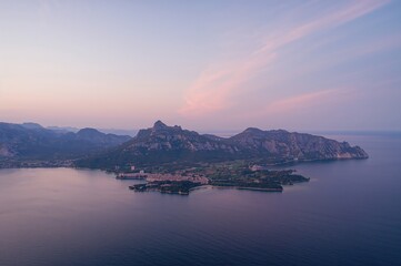 Peaceful bird's-eye perspective of a coastal landscape featuring gentle sky colors merging with the sea and rocky hills, showcasing the area's natural charm