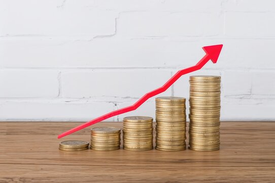 Bar chart made of coin stacks with a declining red line graph against a white wall backdrop on a wooden surface with empty space