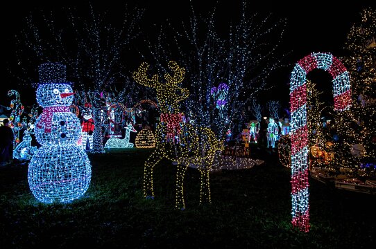 Festive LED display featuring glowing holiday figures such as a snowman, reindeer, and candy cane at an outdoor winter market after dark - Powered by Adobe