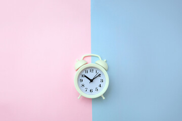 White alarm clock on pink and blue backgrounds. Human circadian rhythms concept. Selective focus and copy space