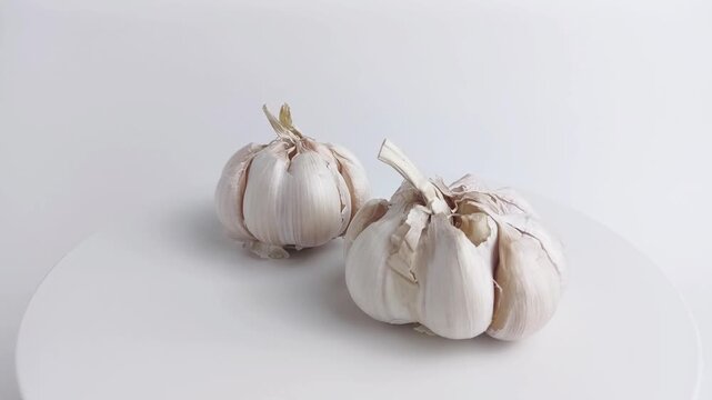 Rotating garlic bulbs on a white podium in seamless video loop. Perfect for food, cooking, spice, health, and clean kitchen concepts.
