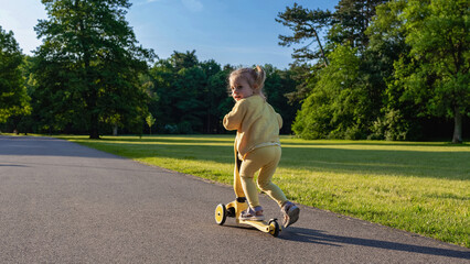 Child scooter riding. Girl yellow scooter park. Motion day lifestyle travel.