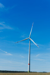 Obraz premium Wind turbine stands tall against a clear blue sky in an open field during a sunny afternoon, symbolizing renewable energy and sustainability