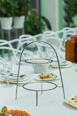 Two-tiered serving stand placed on a dining table with green plants in a bright indoor location