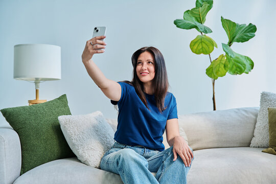 Happy beautiful woman taking selfie portrait on smartphone, at home