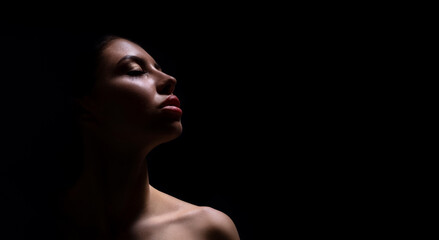 A close-up photograph of a womans face, captured in a dark environment. The woman is facing...