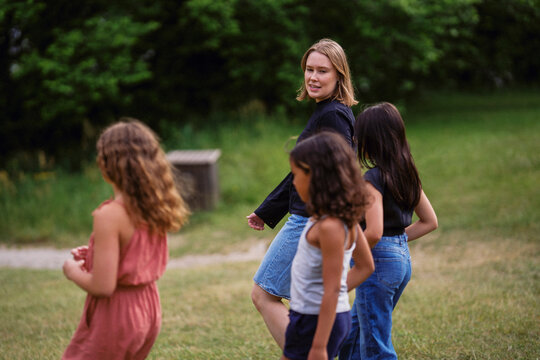 Young female guide talking with girls while walking on playground in summer camp