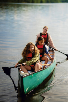 Smiling multiracial girls sitting with female instructor in canoe on lake at summer camp