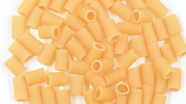 Rotating video of raw Mezze Maniche N84 Italian pasta on white plate. Traditional short tube pasta, authentic Mediterranean cuisine ingredient, dry food concept for cooking and gastronomy.