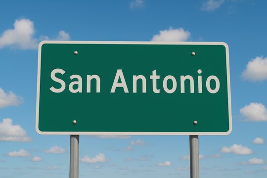 Green highway sign displaying "San Antonio" in white letters, set beneath a bright blue sky with scattered fluffy clouds.