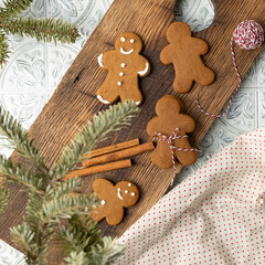 Decorated Gingerbread cookies on a wooden cutting board with cinnamon sticks and red and white twine.