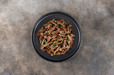 Stir-fry beef marinated with teriyaki sauce, green onions, and sesame seeds on a dark background. Top view