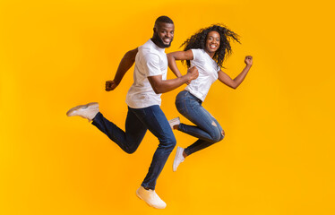 Joyful African American Man And Woman Are Running In The Air, yellow studio background