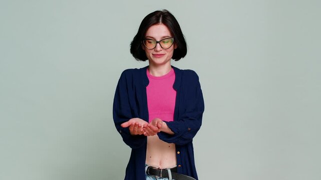 Young woman generously smiles extends hands forward as if offering something free clearly showing kindness generosity. Caucasian girl expresses warm friendly giving gesture isolated on gray background