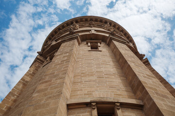 Low-angle exterior view looking up at the sandstone facade and cornice of the historic Wasserturm water tower under a blue cloudy sky in Mannheim, Germany.   © Peeradontax
