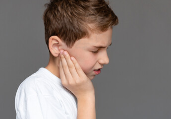 Teenage boy with pained expression holding his sore ears, grey background