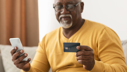 Mature Black Man Shopping Online Using Smartphone And Credit Card Making Payment Via Banking App Sitting On Sofa At Home. Selective Focus On Phone And Bank Card. Cropped, Panorama