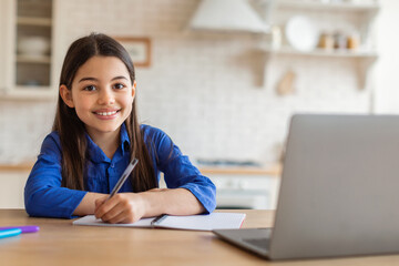 Online Education. Happy Young Girl Taking Notes At Laptop Embracing E-Learning, Studying From Home, Sitting At Desk Doing School Homework. Shot Of Successful Schoolgirl During Digital Class