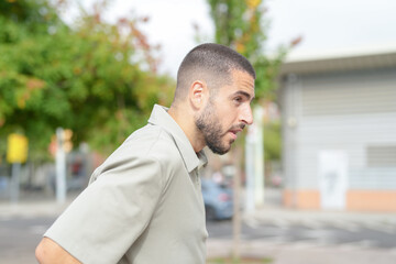 Fototapeta premium A man with a shaved head and a beard is standing on a street. He is wearing a grey shirt and a grey cap