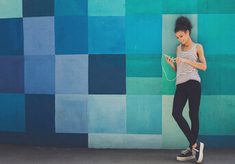 Happy smiling african-american woman leaning on bright blue graffiti wall, while listening music, relaxing from jog training, copy space