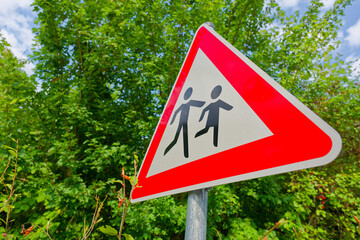 Child crossing warning sign with running figures near trees