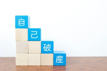 自己破産イメージ。積み木と白背景のコピースペースありの広告素材。