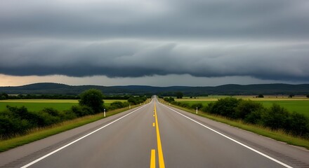 Fototapeta premium Long straight empty road through a rural landscape under a stormy sky