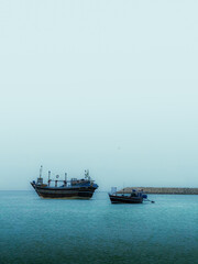 Serene ocean scene with traditional fishing boats gently floating on calm, blue waters under a hazy sky, evoking peace and maritime adventure.