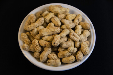 Photograph, one plate of salt peanuts is on a black table background