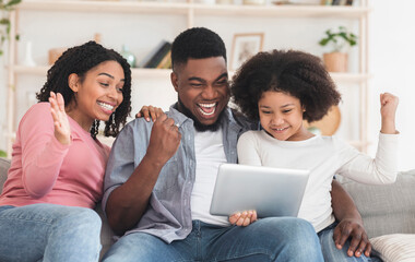Black mother, father and daughter celebrating success with digital tablet, enjoying staying at home together, raising fists in excitement, free space