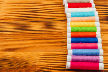 Colorful thread spools arranged on wooden surface for sewing projects
