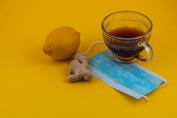 Lemon and ginger tea with a mask on yellow background for health care