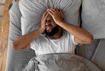 Overhead above top view of young black man suffering from headache or migraine after waking up in...
