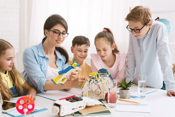 A group of young students are engaged in a STEM class, working together to build a robot. A teacher guides them, while they follow instructions and use their creativity to solve problems.