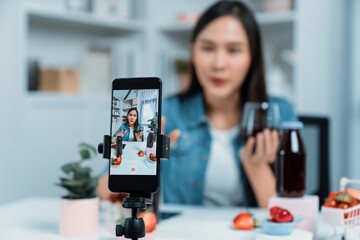 Selective focus smartphone with smiling young beautiful Asian reviewing mixed strawberry and cherry...