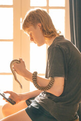 Teenage boy watching mobile phone while holding pet snake