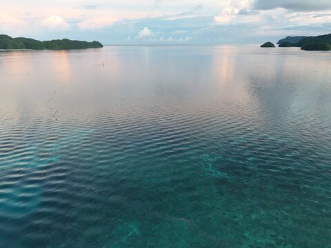 Aerial view of Malakal lagoon in Palau at sunset, calm turquoise sea with coral reef and distant tropical islands. Ngemelachel