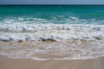 Turquoise sea water wave motion. Summer beach. Calm sea. Seaside resort. Bright sky and waves on beach. Beautiful foamy shoreline. Sea background. Blue ocean. Sandy ocean beach. Sea waves.