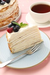 Piece of tasty crepe cake with berries served on pink wooden table, closeup
