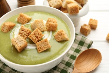 Tasty broccoli cream soup with croutons served on white wooden table, closeup