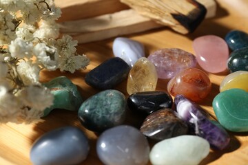 Different beautiful gemstones, palo santo and dried flowers on wooden plate, closeup
