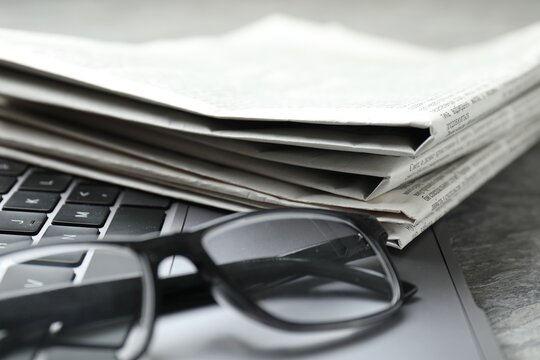 Newspapers, laptop and glasses on grey table, closeup