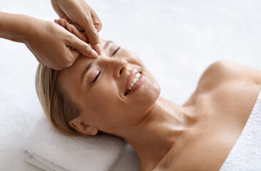 Fototapeta premium Smiling Attractive Middle Aged Woman Receiving Professional Anti-Aging Face Massage At Spa Center, Beautiful Mature Female Lying On Table, Enjoying Wellness And Skincare Treatments, Above View